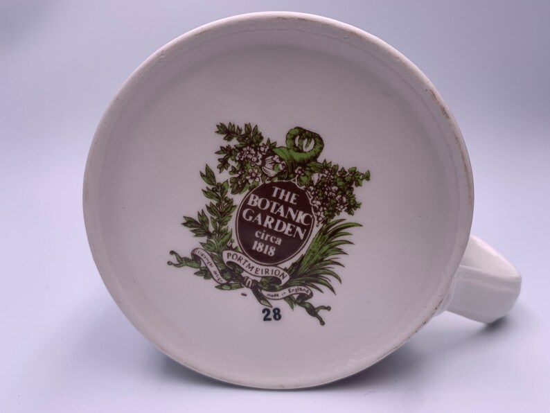 May include: The bottom of a white ceramic mug with a brown and green logo that reads "The Botanic Garden circa 1818 Portmeirion made in England" and the number 28.