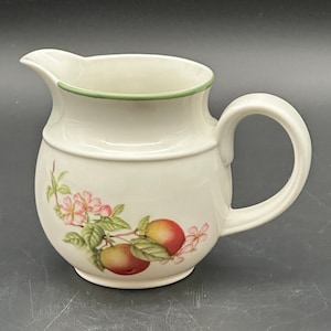 Könnte beinhalten: Weiße Keramik-Milchkanne mit grünem Rand und einem Blumendesign mit rosa Blüten und roten Äpfeln.