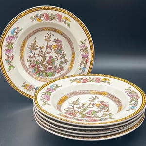 May include: A set of six white ceramic soup bowls with a floral pattern. The bowls have a gold rim and a brown and gold lattice design. The floral pattern features pink, blue, and green flowers and leaves.