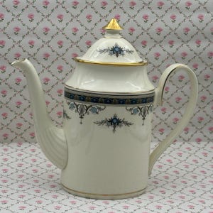 May include: A white porcelain coffee pot with a gold lid and handle. The pot has a blue and gold decorative band and blue floral accents. The spout is curved and the lid has a gold finial. A classic design.