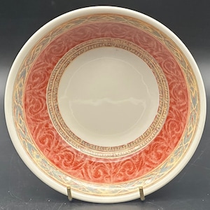 May include: A white ceramic bowl with a red and gold patterned design. The bowl has a wide rim and a deep well.