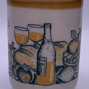 Puede incluir: Una taza de cer&aacute;mica blanca con un borde amarillo y un dise&ntilde;o verde y amarillo de una botella de vino, dos vasos de vino, pan, fruta y fresas.