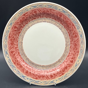 May include: A large, round, white ceramic plate with a red and blue patterned border. The border features a repeating design of stylized leaves and geometric shapes.