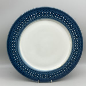 May include: A round ceramic dinner plate featuring a smooth white center and a wide, deep blue rim. The blue border is decorated with two concentric rows of small, raised light gray dots that create a textured pattern around the edge.