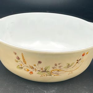 May include: A white ceramic mixing bowl with a floral design featuring brown, orange, and yellow accents. The bowl has two handles on the sides.