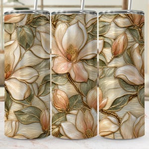 May include: A floral-themed tumbler featuring a repeating pattern of magnolia flowers and leaves. The design incorporates shades of cream, peach, and green, with gold accents. The tumbler has a stainless steel straw.