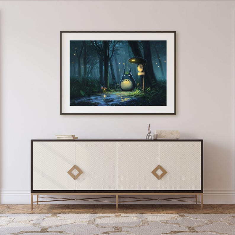 May include: Framed art print featuring a whimsical illustration of a forest scene with a large, round, blue creature with a white belly. The artwork is set in a dark, misty forest with a path and glowing lights, creating a magical atmosphere.