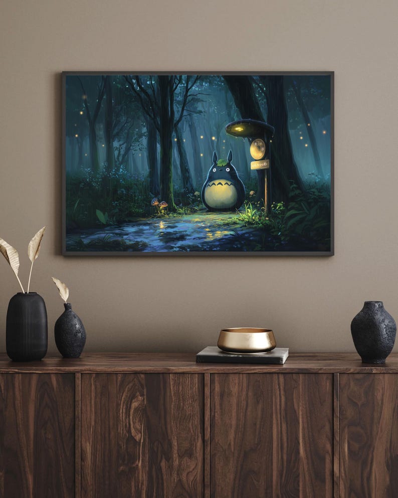 May include: Framed art print featuring a whimsical forest scene with a large, round, dark blue creature with a white belly. The artwork depicts a path, trees, and glowing lights, creating a magical atmosphere. The print is displayed above a wooden cabinet.