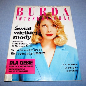 Może przedstawiać: Okładka magazynu z kobietą w jasnoniebieskiej marynarce i czerwonej szmince. Tytuł magazynu to "BURDA INTERNATIONAL" w kolorze różowym. Na okładce widnieją napisy "Świat wielkiej mody" i "DLA CIEBIE".