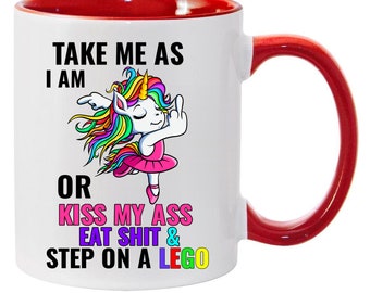 May include: White ceramic coffee mug with a red rim and handle. The mug features a colorful cartoon unicorn with a middle finger raised and the text "TAKE ME AS I AM OR KISS MY ASS EAT SHIT & STEP ON A LEGO".