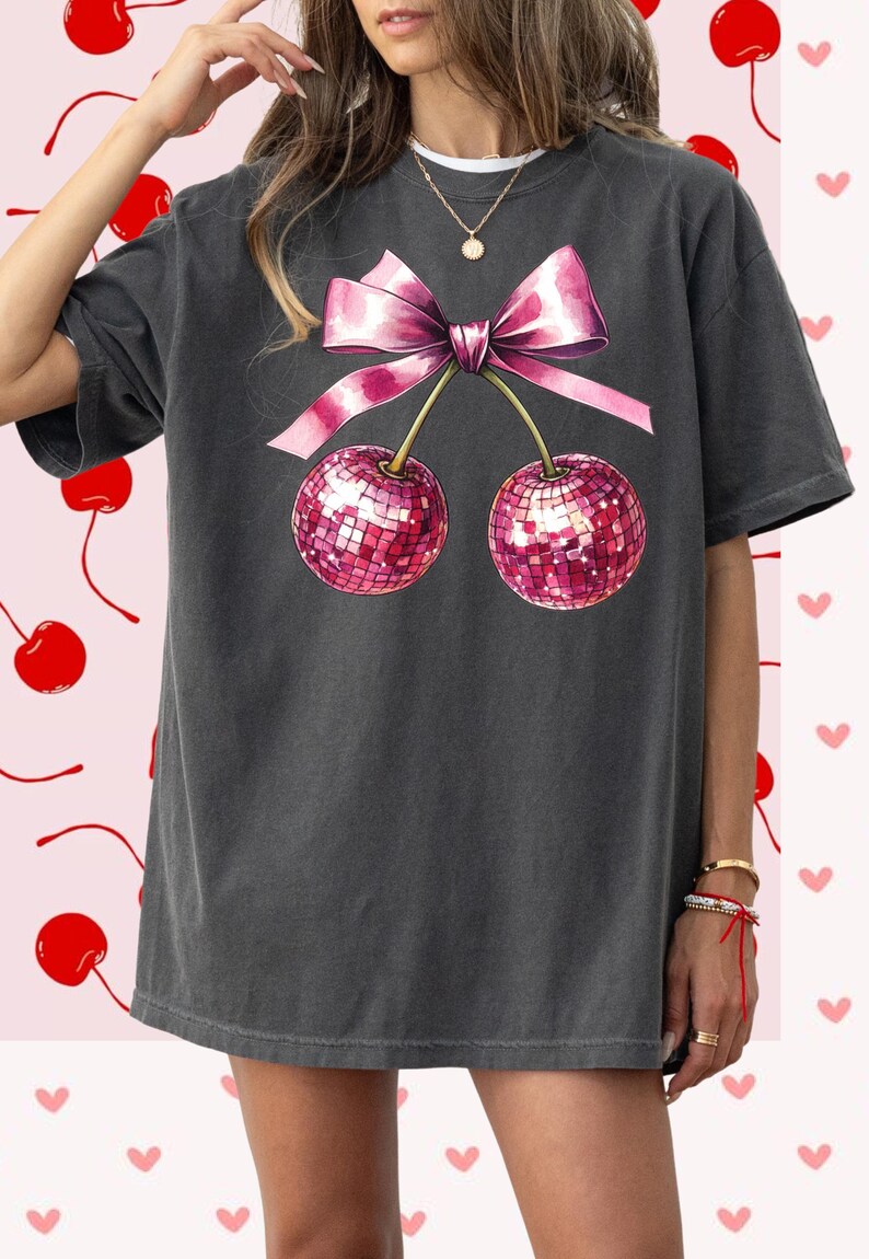 May include: An oversized charcoal grey t-shirt featuring a pink bow and two pink cherries with sequins. The cherries are on stems and the bow is tied around the stems.