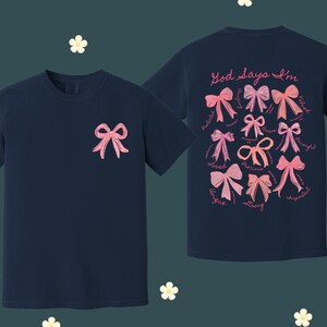 May include: Two navy blue t-shirts with pink bows and the text "God says I'm" with a list of positive words. The words include: loved, unique, precious, strong, gifted, valued, thoughtful, and supported.