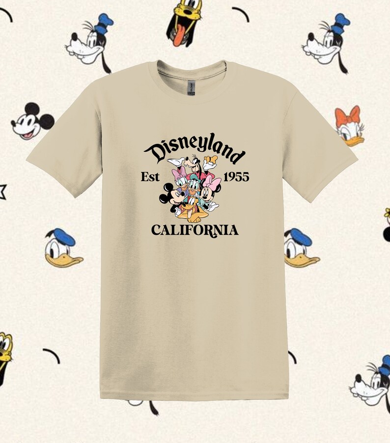 May include: A beige t-shirt with a black graphic of Mickey Mouse, Minnie Mouse, Donald Duck, Goofy, and Pluto. The graphic includes the text "Disneyland Est 1955 CALIFORNIA".