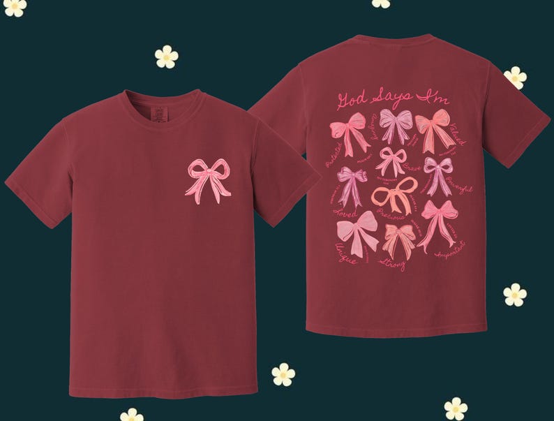 May include: Two maroon t-shirts with pink bows and the text "God Says I'm" on the front. The shirt on the right has a variety of pink bows with words like "loved", "strong", and "beautiful" around them.