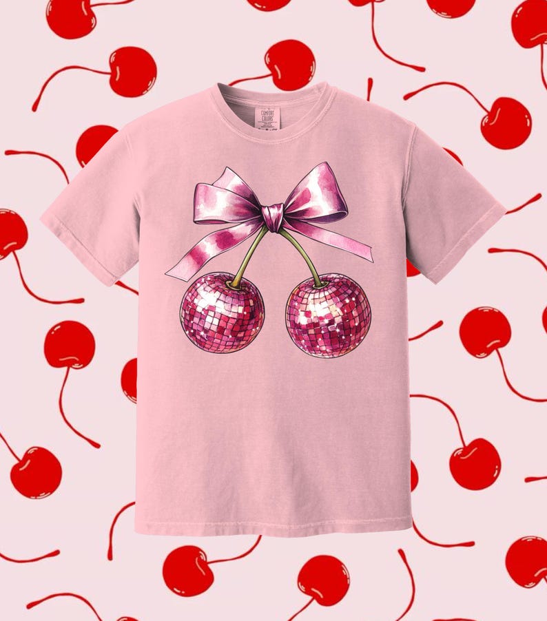 May include: Pink t-shirt featuring a graphic of two cherries with a pink bow. The cherries are sparkly and have a disco ball effect.