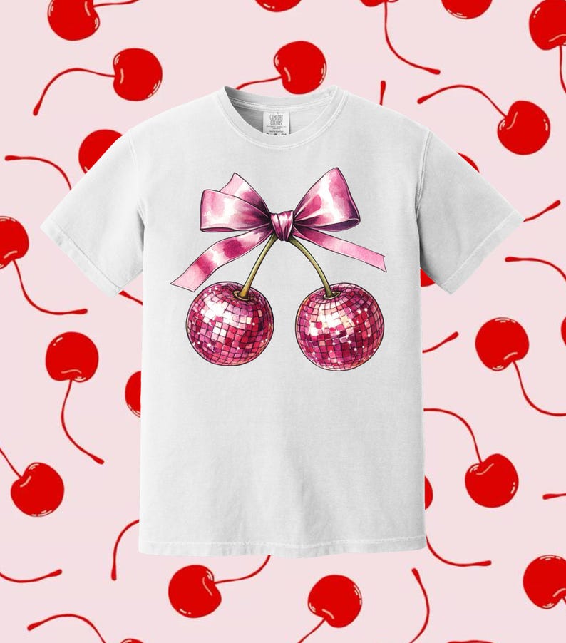 May include: White t-shirt featuring a pink bow and two cherries with sparkly red accents.