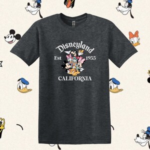 May include: A dark heather grey t-shirt with a white graphic of Mickey Mouse, Minnie Mouse, Donald Duck, Goofy, Pluto, and Daisy Duck. The graphic includes the text "Disneyland Est 1955 California".