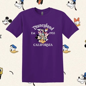 May include: Purple t-shirt with a white graphic of Mickey Mouse, Minnie Mouse, Donald Duck, Goofy, and Pluto. The graphic includes the text "Disneyland Est 1955 CALIFORNIA".