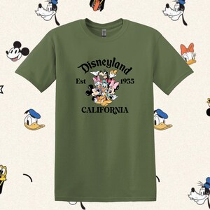 May include: A green t-shirt with a black graphic of Mickey Mouse, Minnie Mouse, Donald Duck, Goofy, Pluto, and a cartoon dog. The graphic includes the text "Disneyland Est 1955 California".