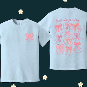 May include: Two light blue t-shirts with pink bows and the text "God says I'm" with a list of positive words around the bows on the back.