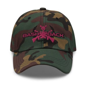 May include: Camouflage baseball cap with a pink embroidered logo that says "Bash Back" with crossed rifles and a wreath.
