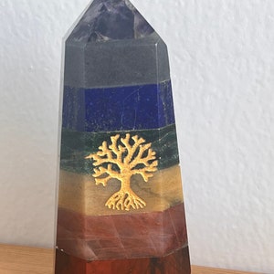 Puede incluir: Una pirámide de cristal de siete capas con un diseño de árbol de la vida dorado. Las capas son amatista, sodalita, lapislázuli, aventurina verde, citrino, cornalina y jaspe rojo.