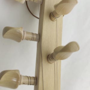 Puede incluir: Un clavijero de instrumento musical de madera clara con seis clavijas de afinaci&oacute;n talladas y lisas dispuestas en dos filas. Cuerdas met&aacute;licas finas est&aacute;n enrolladas alrededor de las clavijas a lo largo del m&aacute;stil del instrumento.
