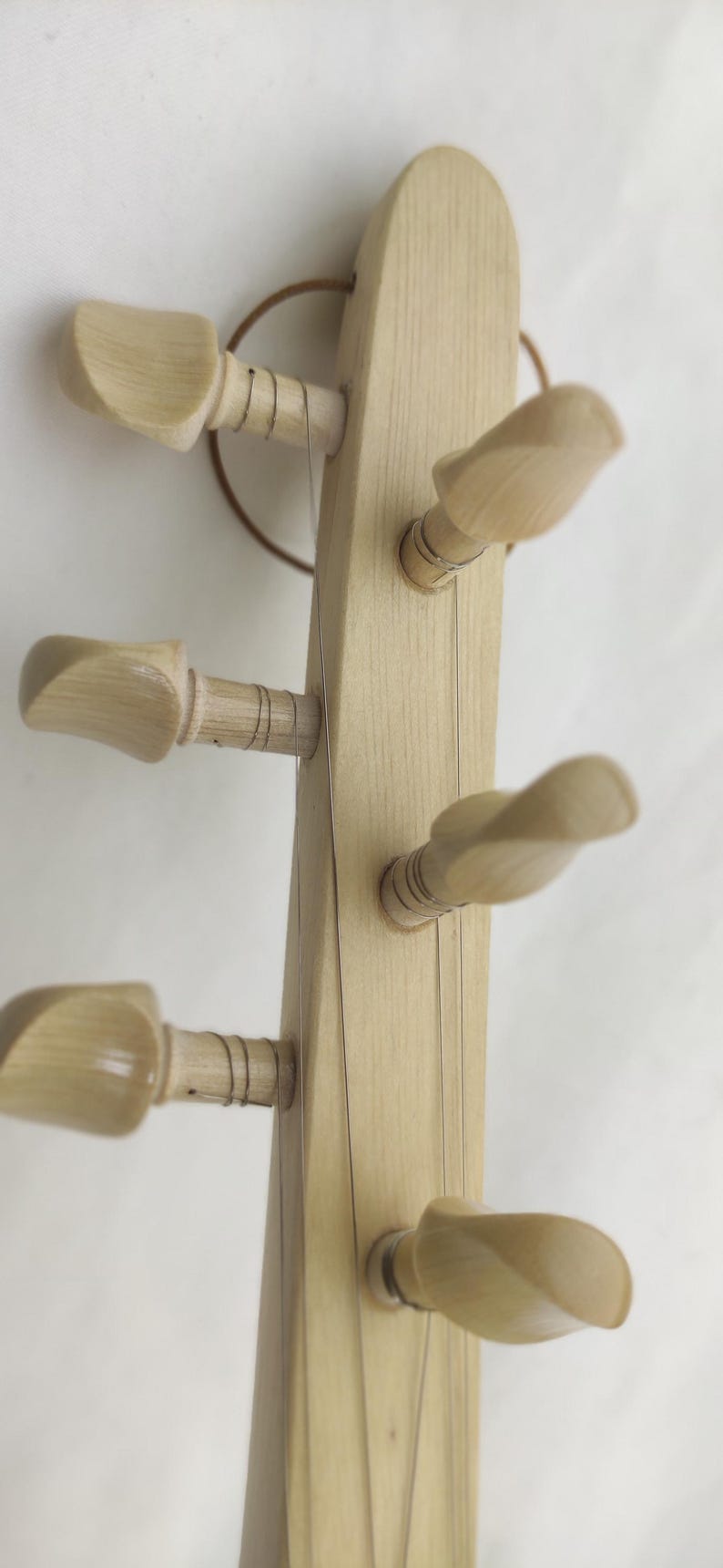 Puede incluir: Un clavijero de instrumento musical de madera clara con seis clavijas de afinaci&oacute;n talladas y lisas dispuestas en dos filas. Cuerdas met&aacute;licas finas est&aacute;n enrolladas alrededor de las clavijas a lo largo del m&aacute;stil del instrumento.