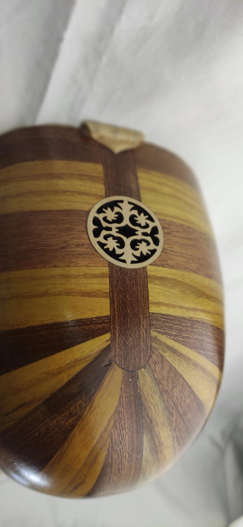 Puede incluir: Un cuerpo de instrumento musical de madera redondeado con paneles de vetas de madera alternas en marr&oacute;n claro y oscuro. Una incrustaci&oacute;n circular de madera clara con un patr&oacute;n de corte sim&eacute;trico e intrincado est&aacute; centrada.