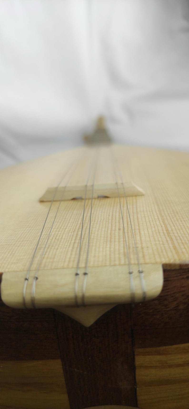Puede incluir: Un instrumento musical de cuerda con una caja de resonancia de madera clara y veta visible. Seis cuerdas met&aacute;licas finas recorren verticalmente el cuerpo, pasando sobre un puente de madera y ancladas en un cordal de madera clara.