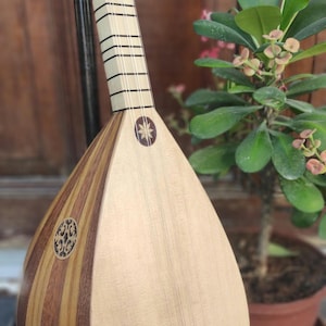 Puede incluir: Un instrumento musical de cuerda con un cuerpo en forma de pera hecho de duelas de madera clara y oscura. Presenta un m&aacute;stil largo con trastes negros, una boca circular con una incrustaci&oacute;n intrincada y una incrustaci&oacute;n en forma de estrella.