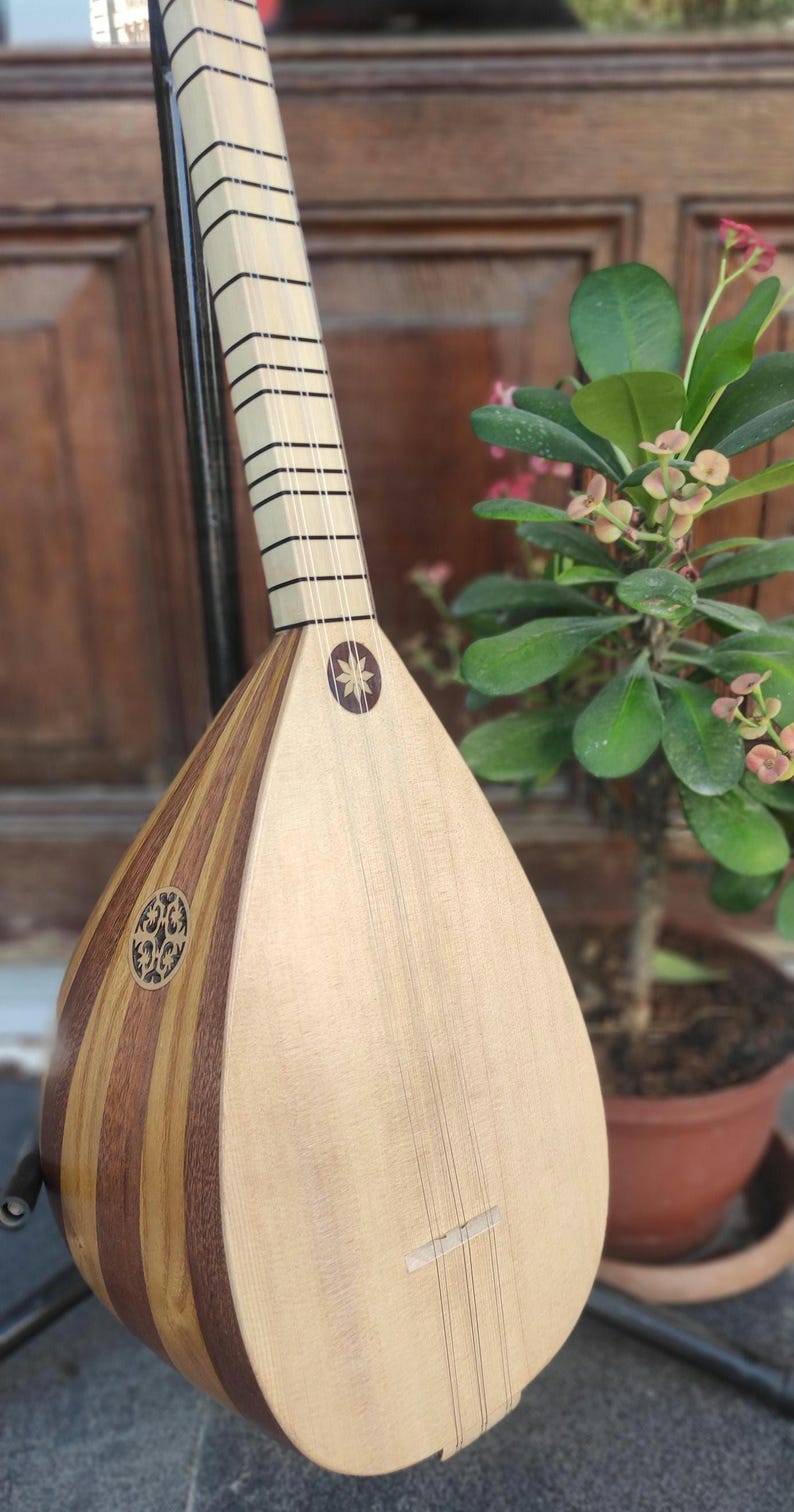 Puede incluir: Un instrumento musical de cuerda con un cuerpo en forma de pera hecho de duelas de madera clara y oscura. Presenta un m&aacute;stil largo con trastes negros, una boca circular con una incrustaci&oacute;n intrincada y una incrustaci&oacute;n en forma de estrella.