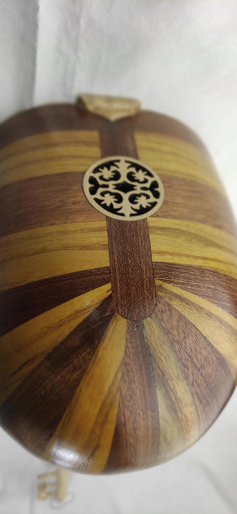 Puede incluir: Un cuerpo de instrumento musical de madera con una parte posterior redondeada en forma de cuenco, construida con duelas de madera alternas en marr&oacute;n oscuro y bronceado claro. Un roset&oacute;n circular de madera cortado con l&aacute;ser y dise&ntilde;o floral.