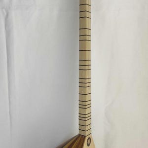 Puede incluir: Un instrumento de cuerda de m&aacute;stil largo con un cuerpo en forma de pera hecho de segmentos de madera clara y oscura alternados. Presenta una tapa arm&oacute;nica de madera clara, un m&aacute;stil largo con varios trastes y un clavijero con seis clavijas.
