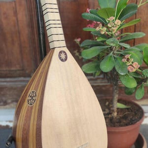 Puede incluir: Un instrumento musical de cuerda con un cuerpo en forma de pera hecho de segmentos de madera clara y oscura. Presenta un m&aacute;stil largo con trastes, una boca circular con una incrustaci&oacute;n intrincada y una incrustaci&oacute;n en forma de estrella.