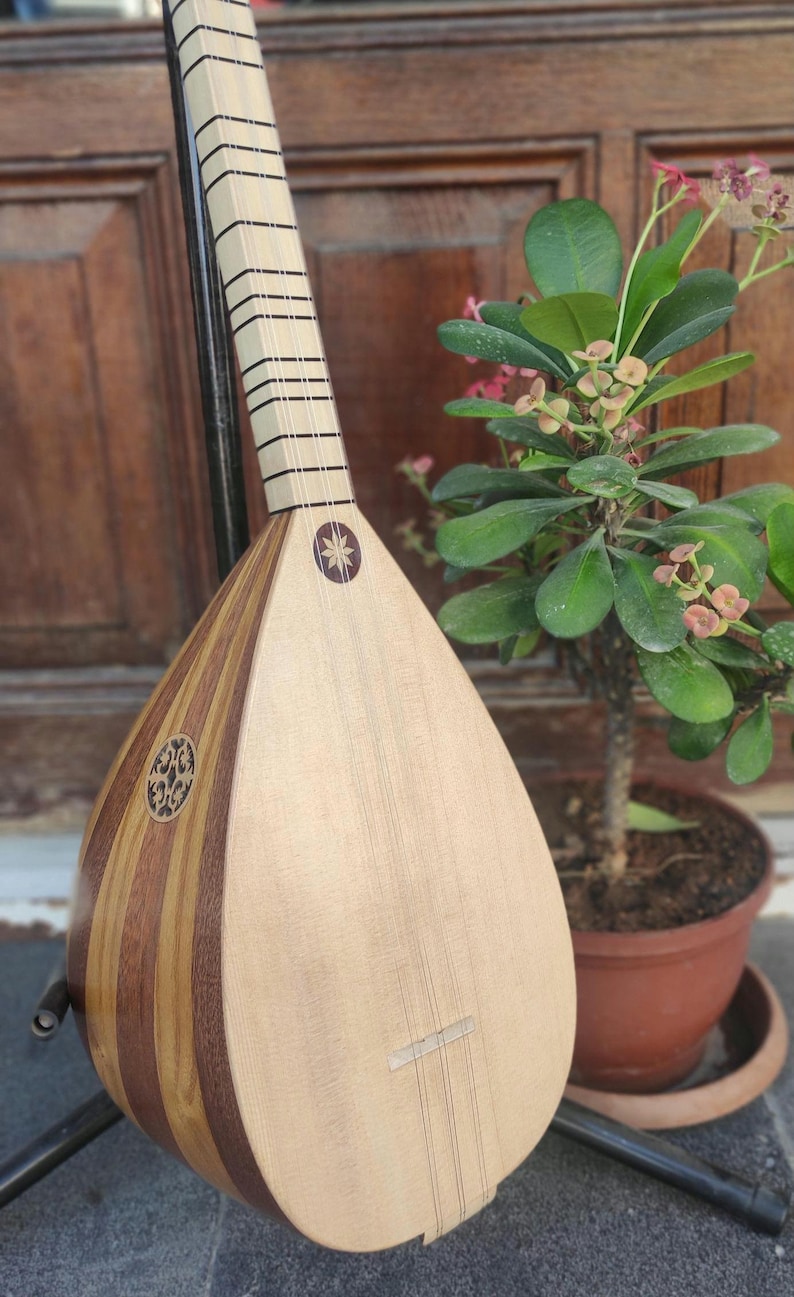 Puede incluir: Un instrumento musical de cuerda con un cuerpo en forma de pera hecho de segmentos de madera clara y oscura. Presenta un m&aacute;stil largo con trastes, una boca circular con una incrustaci&oacute;n intrincada y una incrustaci&oacute;n en forma de estrella.
