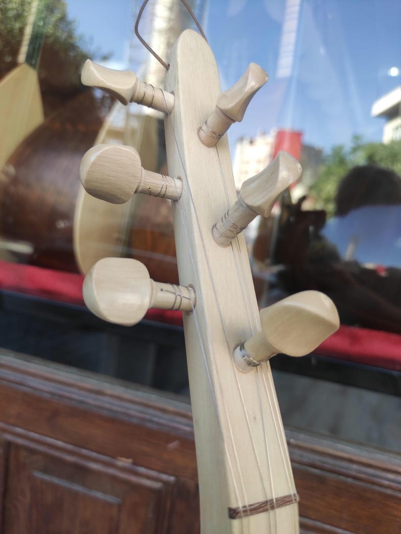 Puede incluir: Un clavijero de madera de color claro de un instrumento musical de cuerda con seis clavijas de afinaci&oacute;n dispuestas en tres pares a los lados. Se aprecia la veta de la madera lisa y p&aacute;lida, con cuerdas finas sujetas a las clavijas.