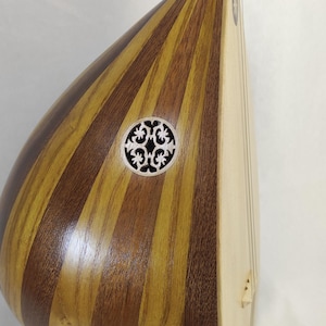 Puede incluir: Un instrumento musical de cuerda con un cuerpo en forma de pera construido con duelas de madera clara y oscura alternadas. Presenta una boca circular con una roseta tallada de patr&oacute;n floral intrincado y un m&aacute;stil largo con trastes negros.