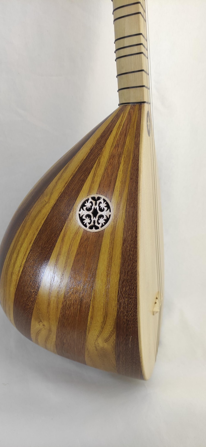 Puede incluir: Un instrumento musical de cuerda con un cuerpo en forma de pera construido con duelas de madera clara y oscura alternadas. Presenta una boca circular con una roseta tallada de patr&oacute;n floral intrincado y un m&aacute;stil largo con trastes negros.