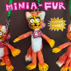 May include: Three orange and white plush fox keychain figures with black eyes and a red bandana. The middle fox is facing forward, while the other two are facing to the sides. The text "CUSTOM MADE!" is on a gold starburst sticker in the background.