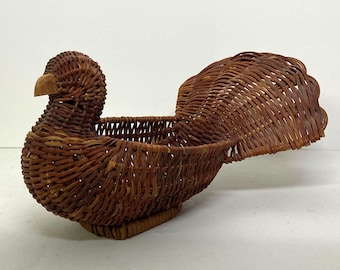 May include: A handcrafted, brown wicker basket shaped like a bird. The bird has a detailed woven body, a wooden beak, and a fanned tail. The basket is designed to hold items and is suitable for decorative use.