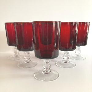 May include: A white ceramic mug with a black handle and the text "But First, Coffee" in a bold, black font. The mug is set against a blurred background, suggesting a cozy setting.