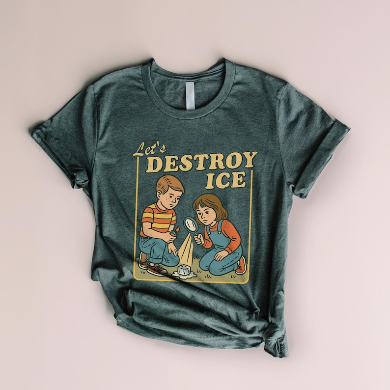 May include: Dark teal t-shirt featuring a retro illustration of two children examining a melting ice cube with a magnifying glass. The text "Let's DESTROY ICE" is in a yellow rectangular frame. The children are wearing vintage-style clothing.