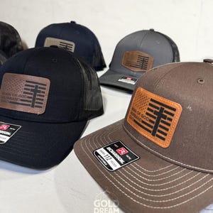 May include: Several baseball caps in black, navy, and brown with a mesh back. Each cap features a leather patch with the text "MAN OF GOD, HUSBAND, DAD" and a cross design. The caps are adjustable and have a Richardson tag.