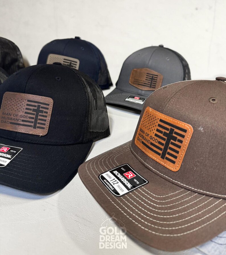 May include: Several baseball caps in black, navy, and brown with a mesh back. Each cap features a leather patch with the text "MAN OF GOD, HUSBAND, DAD" and a cross design. The caps are adjustable and have a Richardson tag.