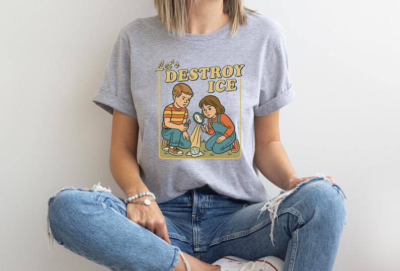 May include: A light gray t-shirt featuring a retro illustration of two children with magnifying glasses, melting a cube of ice. The text "Let's DESTROY ICE" is above the children in a yellow box.