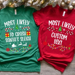 May include: Two Christmas themed t-shirts. The green shirt says "Most Likely to Crash Santa's Sleigh" with a Christmas tree, candy canes, snowflakes, and presents. The red shirt says "Most Likely Custom Text" with a Christmas tree, candy canes, snowflakes, and ornaments.