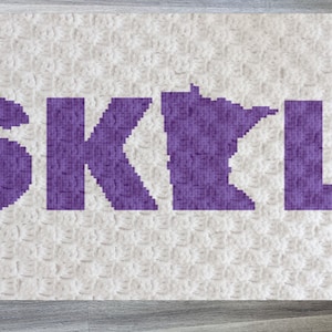 May include: A white crocheted blanket with the word "SKIL" in purple letters, with the letter "I" replaced by the outline of the state of Minnesota.