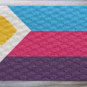 May include: A crocheted flag with a white triangle containing a yellow heart, a blue stripe, a pink stripe, and a purple stripe.