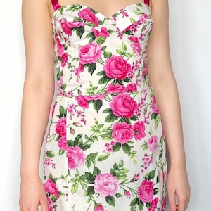 May include: A white dress with a pink floral print and pink ribbon straps. The dress has a fitted bodice and a flared skirt.